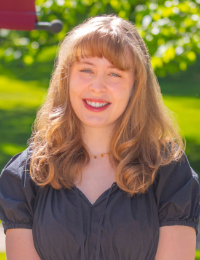 Headshot of young blonde woman in dark blouse