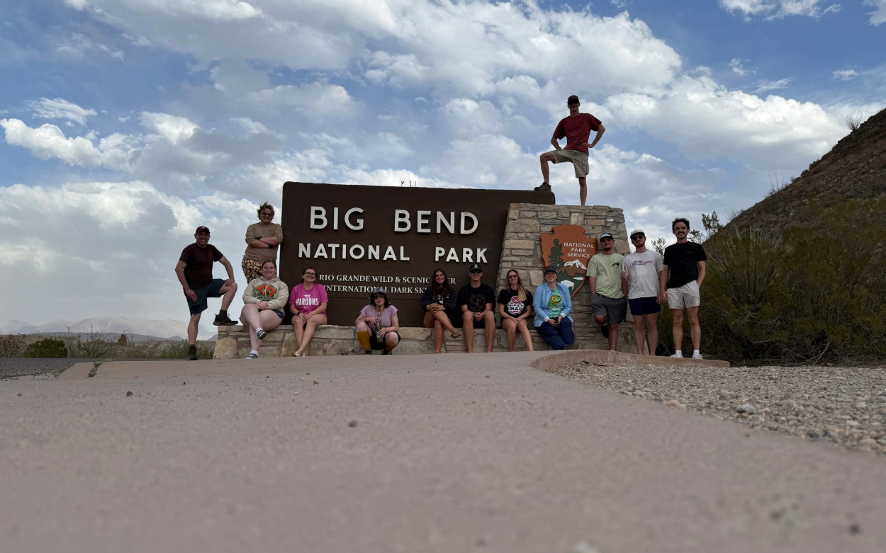 Students sit in front of and stand on the sign for Big Bend National Park in Texas.