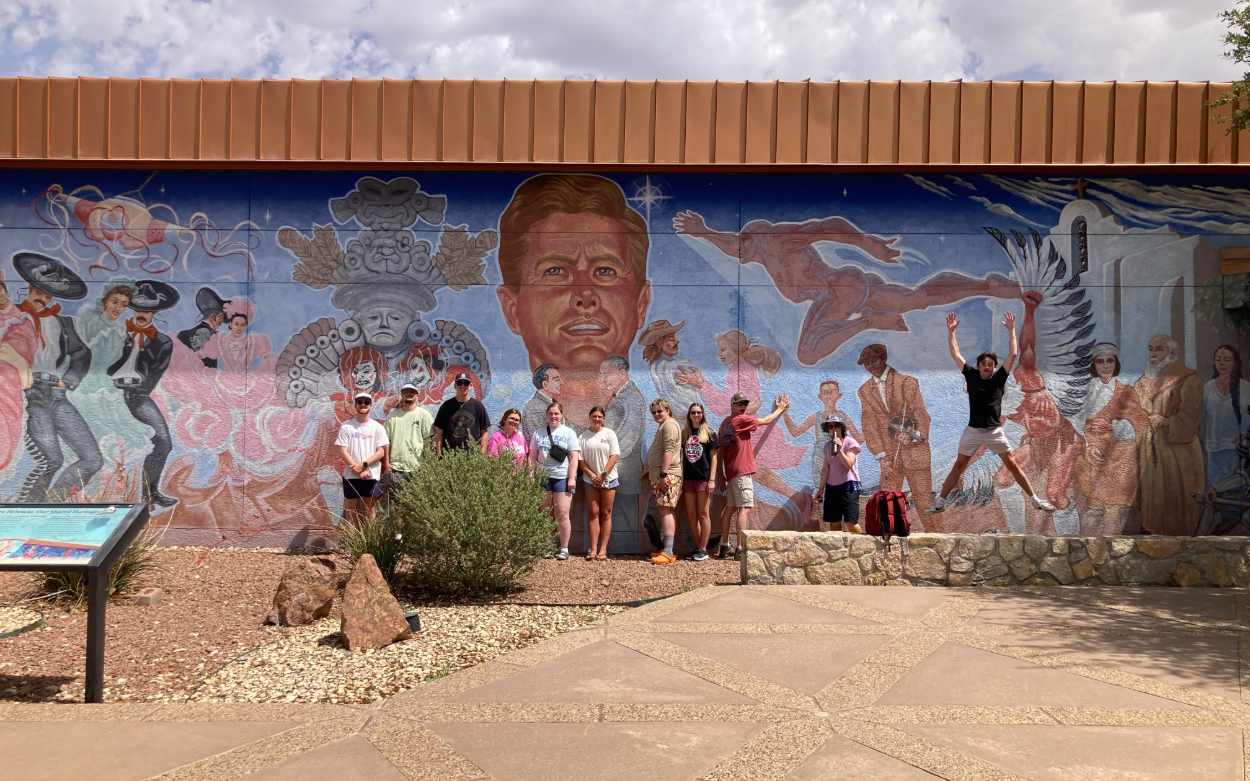 Students pose in front of a colorful mural titled "Nuestra Herencia" at Chamizal National Memorial Cultural Center. The mural depicts images symbolizing the blending of cultures between the United States and Mexico. 