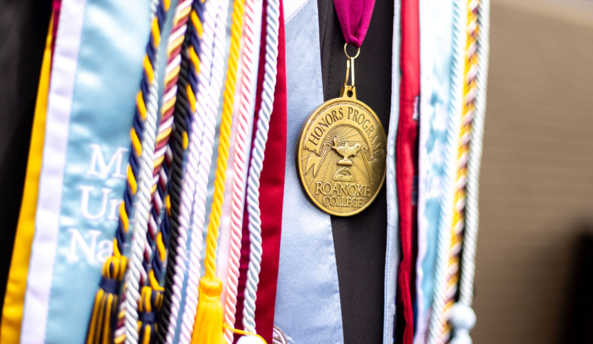 Detail shot of multicolored cords and sashes with a gold medal in the center that says "Honors Program."
