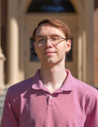 Headshot of young man with brown hair and glasses in a pink polo shirt