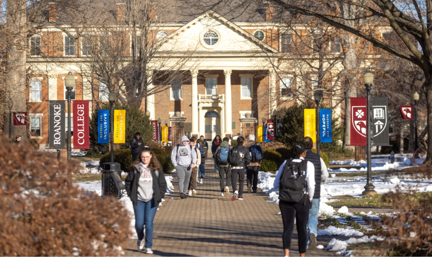 Students walk up a sidewalk with a historic brick campus building in the background.