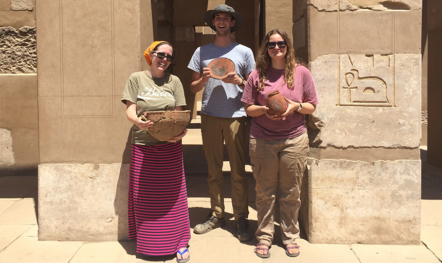 A professor and two students hold up ceramic pottery works