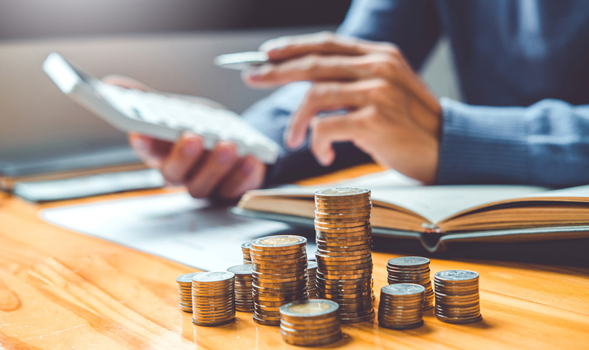 stacks of coins with a person in background holding a calculator