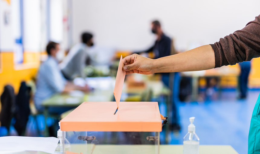 a person's hand is seen placing a paper into a ballot box