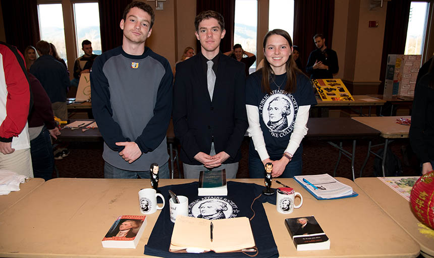 Three students stand over a table with a t shirt and books on the table