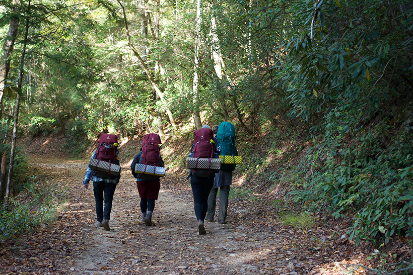 Students walking away on hiking trail with packs on