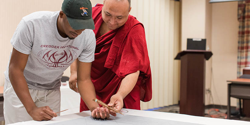 A Tibetan Monk helping a student with the student sand mandala