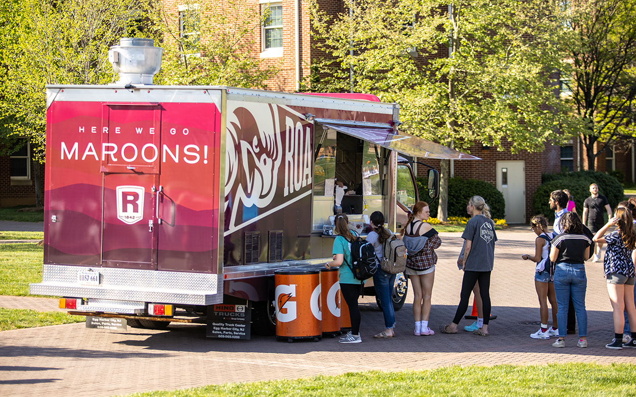 A maroon food truck with a line of students waiting at the window.