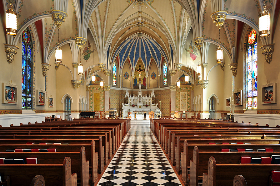 The gilt interior of St. Andrews Catholic Church, looking down the center aisle with pews on either side.
