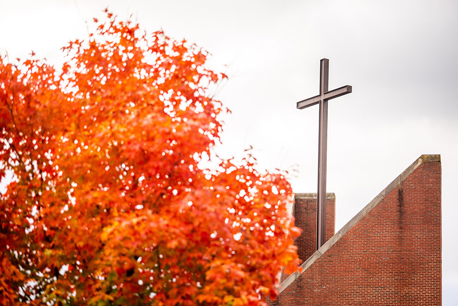 The cross on top of Antrim Chapel visible against a grey sky with yellow trees in foreground.