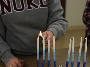 A student lighting the first candle of a menorah