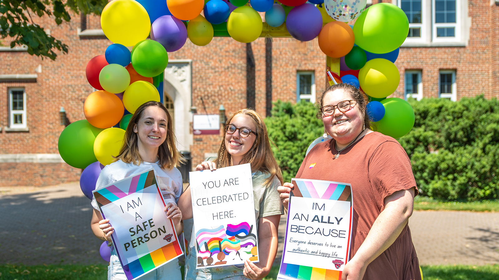 3 students on campus with multi-colored balloons