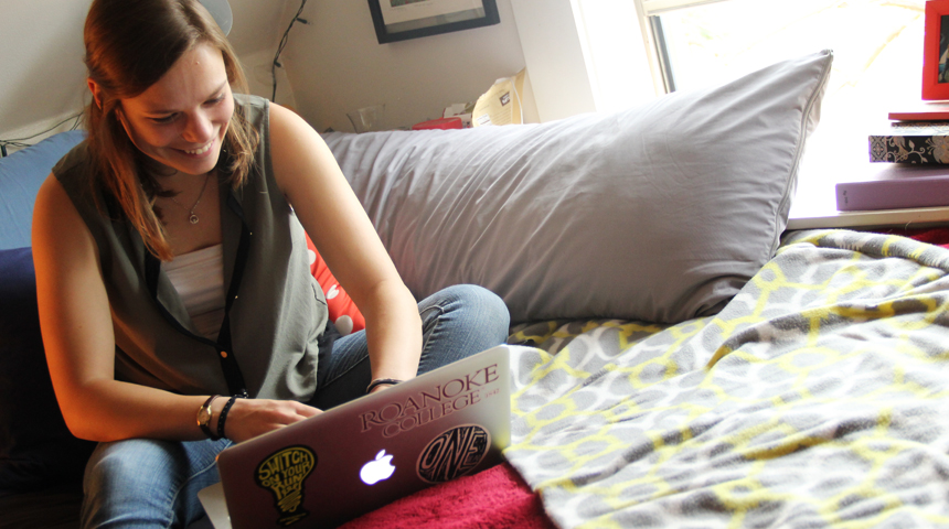 student sitting on a bed with a laptop