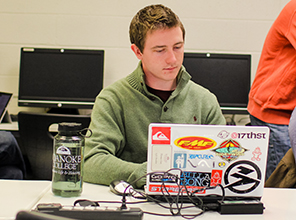 A male student sitting at a laptop working on research in a computer lab