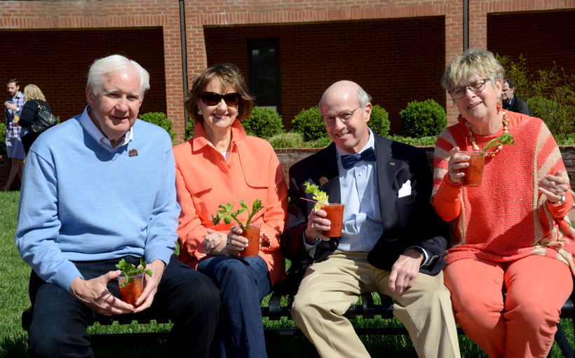 Four alumni pose for a picture sitting on a bench in front of Olin.