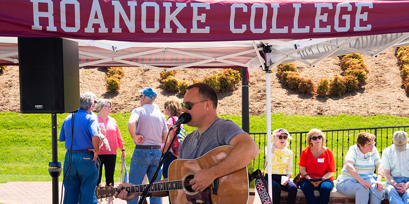 Man plays guitar under a tent that says Roanoke College