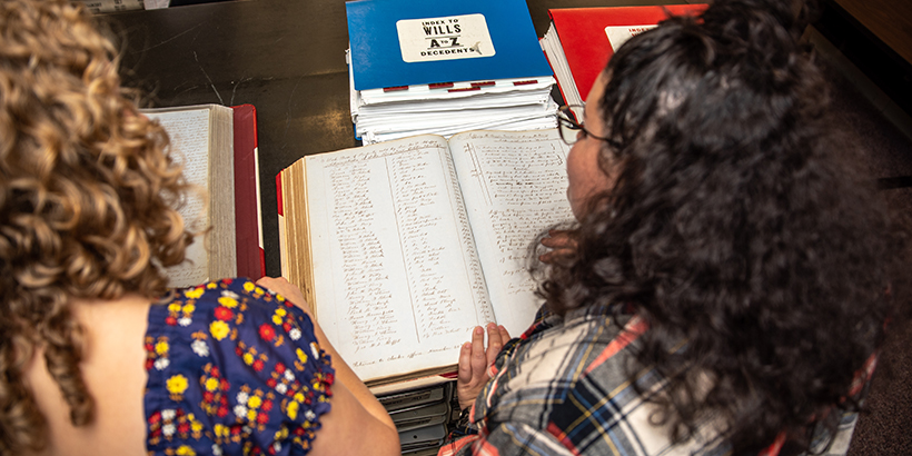 two student researchers look over a handwritten record book