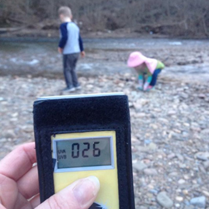 hand holding light meter with children in the background along a river