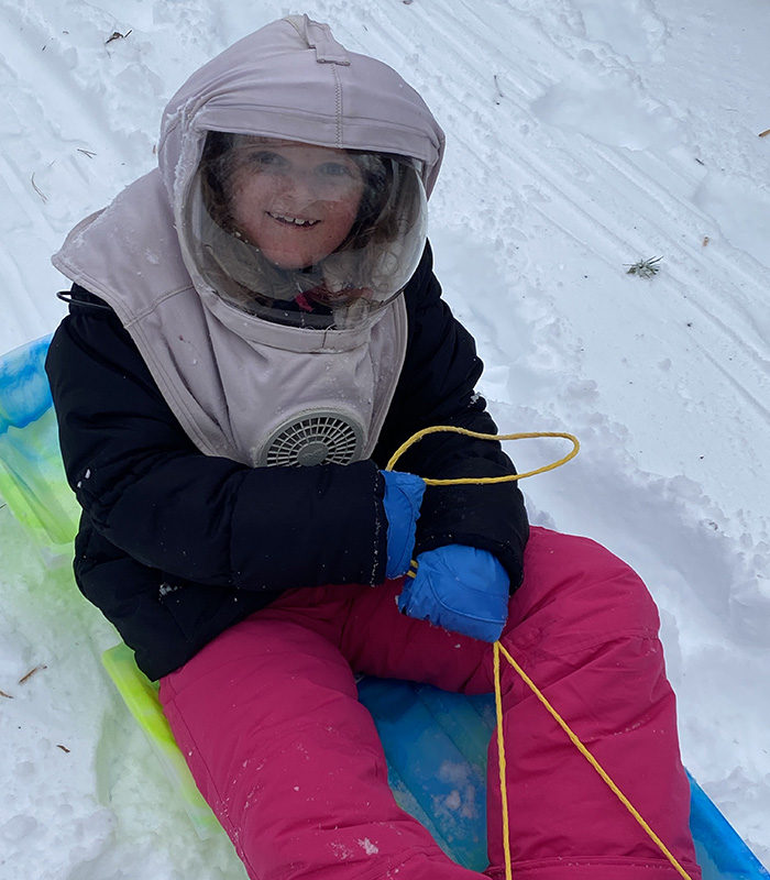 girl on sled wearing protective hat with face shield and fan