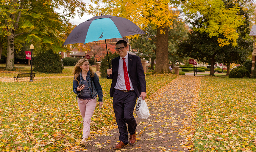 Students walk on campus holding an umbrella on a rainy fall day