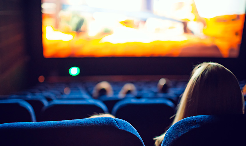 Image of people seated in a movie theater looking at the lighted screen ahead of them