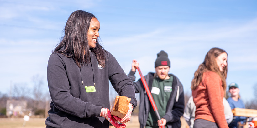 A student volunteer smiles while helping move bricks