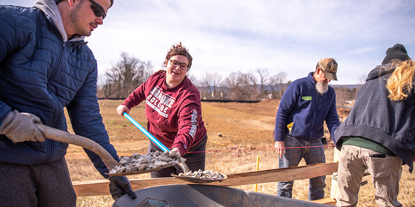Students shovel gravel and carry wooden fence beams
