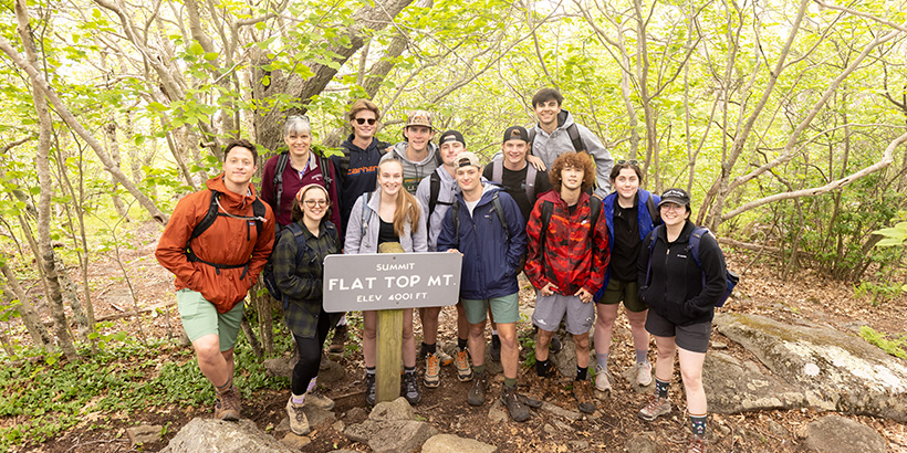 Students gather around a wooden sign that reads: Summit, Flat Top Mountain, Elevation 4,001 Feet