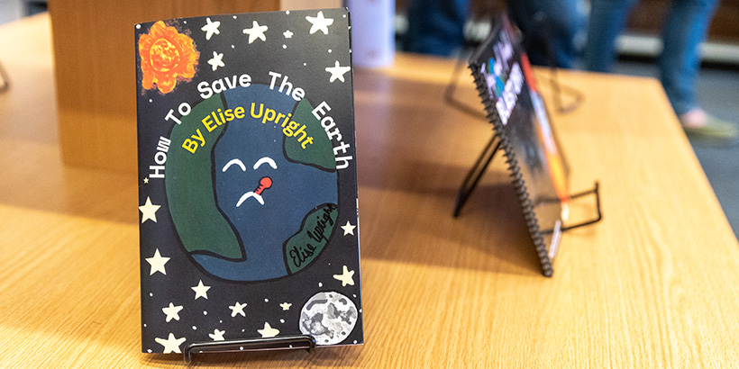 Close-up image of one of the student books with the title, How to Save the Earth, and cover art of an illustration showing a sad planet earth using a thermometer to take its temperature