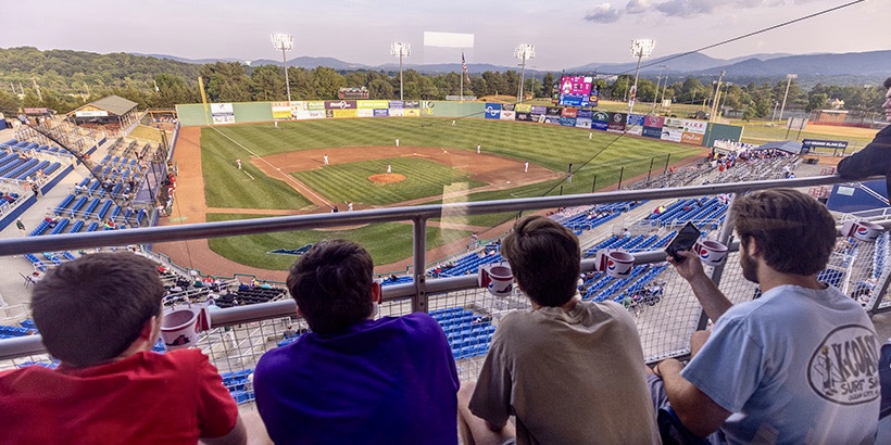 Students sit in the outdoor seats of a stadium suite at the Salem Red Sox while watching the game on the baseball field below
