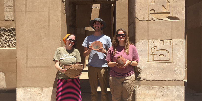 A professor and two students hold ceramic pottery while posing for a picture