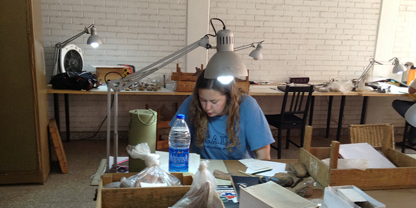 A student leans over her work station with a swivel lamp shining overhead