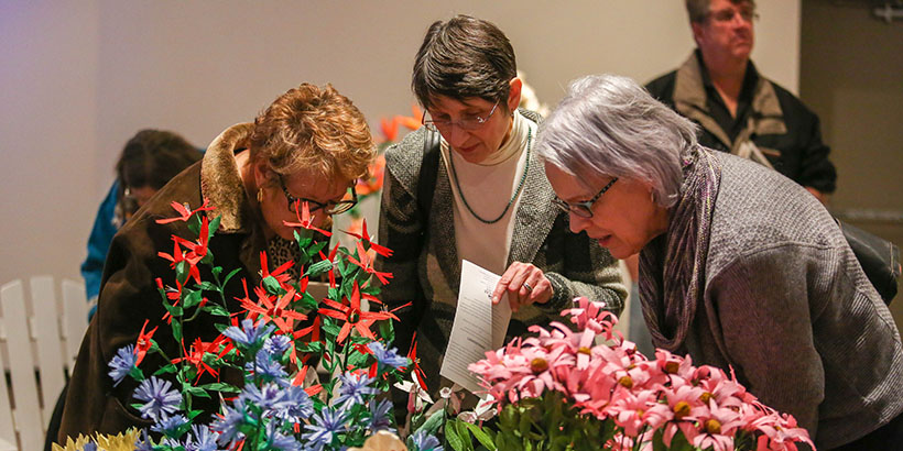 three women look up close at the blue, pink and red flowers