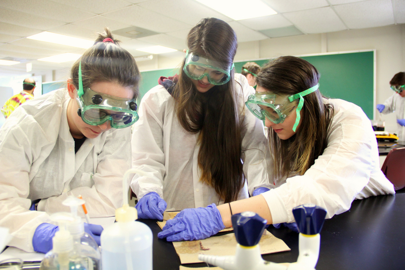 Three students in chemistry lab wearing gloves and goggles