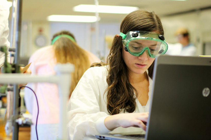 Student in chemistry lab wearing goggles looking at computer
