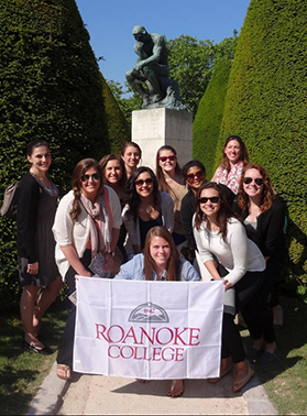 Students posing in front of a sculpture with a roanoke college banner