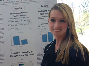 A student standing in front of her research poster at a presentation