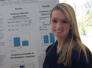 A student standing in front of her research poster at a presentation