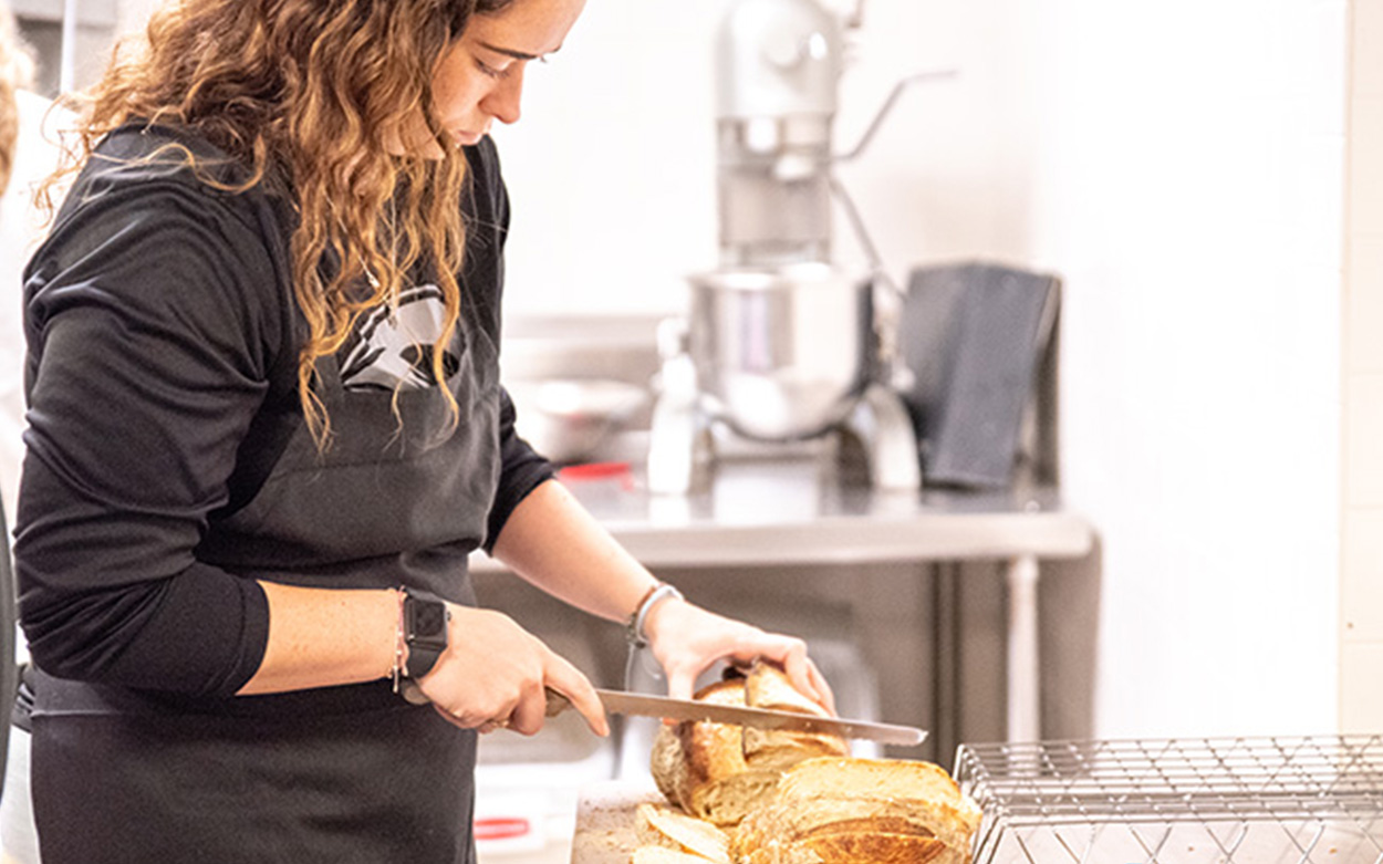 A student uses a knife to slice a fresh baked loave of bread